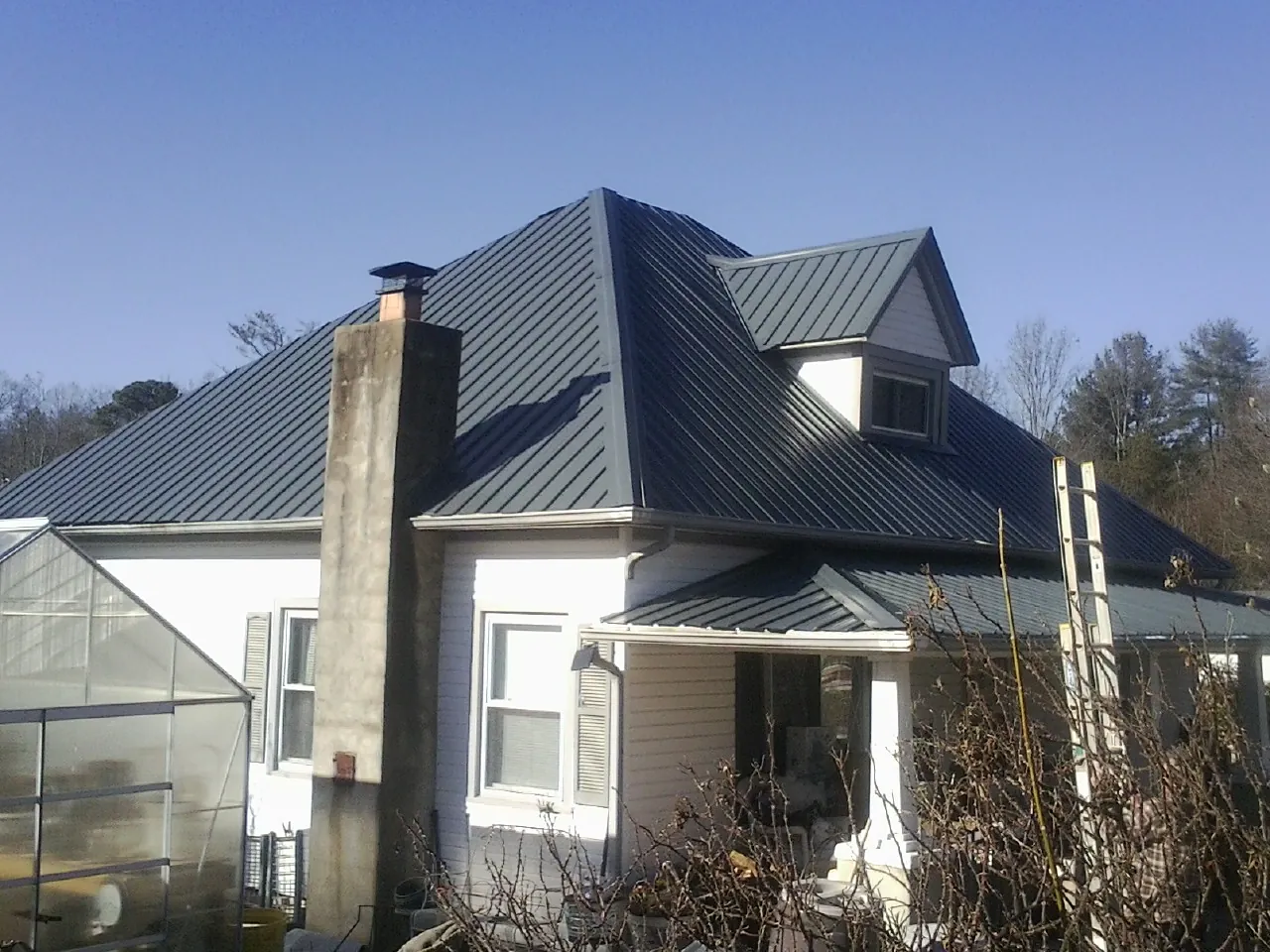 Dark blue standing seam metal roof on a white farmhouse with dormer — Slate & Tile Roof Repair by Roofing Brothers in Moonachie