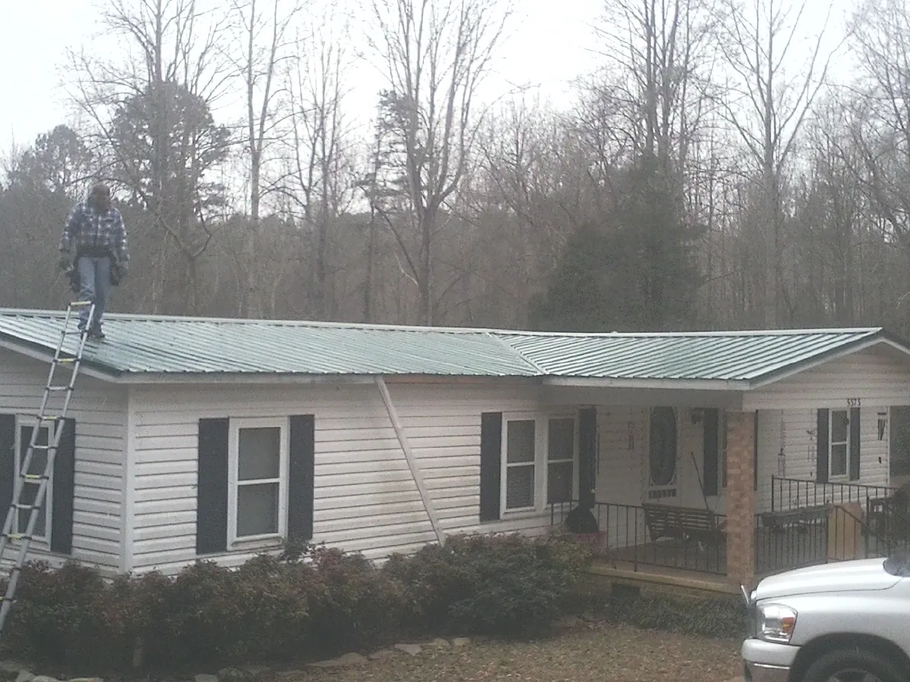 Worker on a ladder beside a new green metal roof on a ranch home in Moonachie