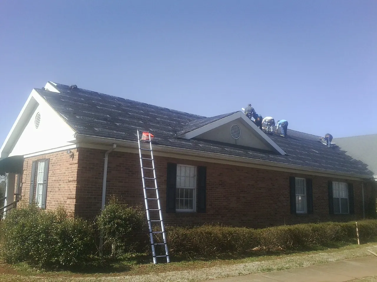 Crew tearing shingles off a brick ranch roof with a ladder set — Emergency Roof Repair work by our crew in Moonachie