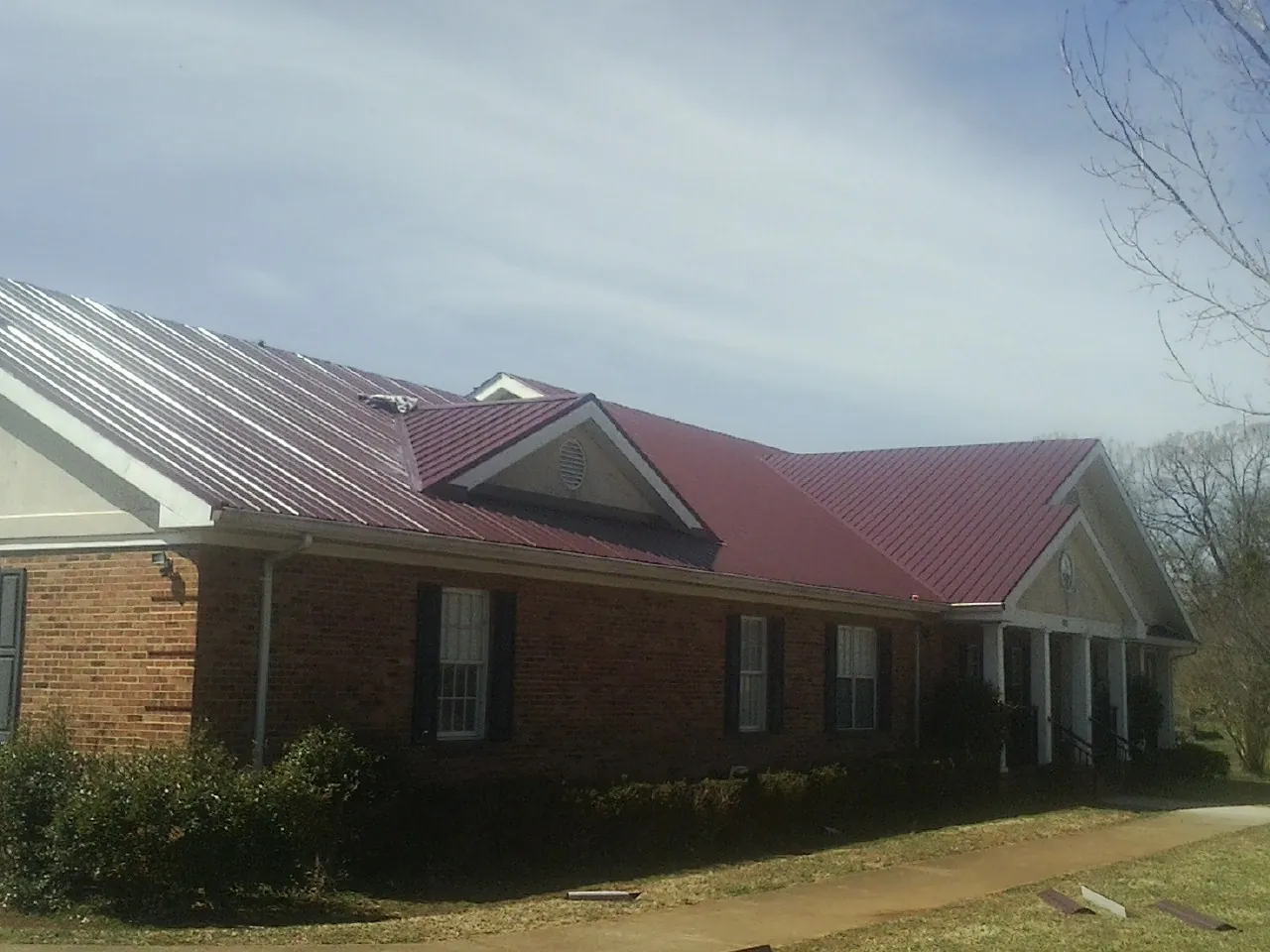 Red metal roof with gabled entries on a long brick building, from a Hail Damage Roof Repair job in Moonachie