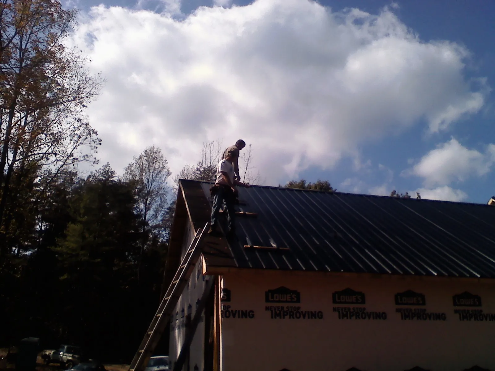 Roofer fastening dark metal panels high against a cloudy sky, from a Roof Inspection job in Moonachie