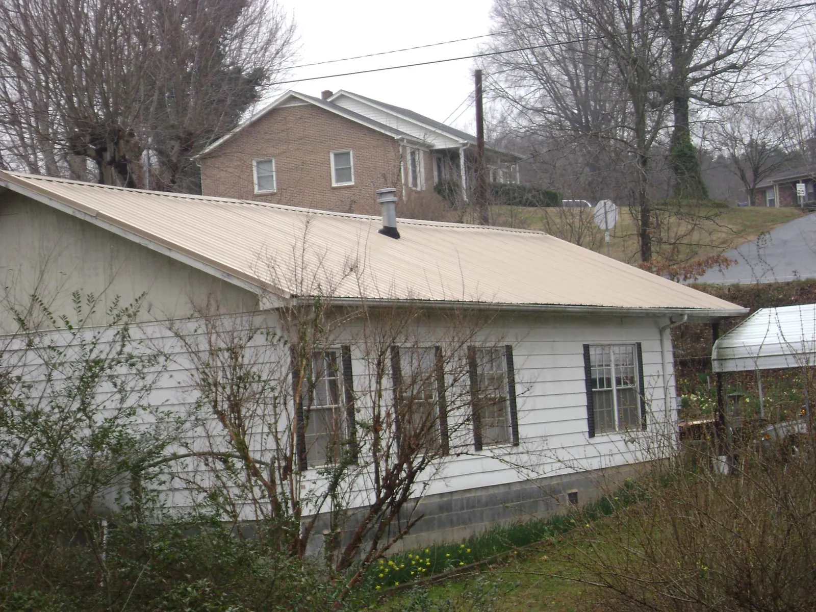 Tan metal roof on a white sided house set into a hillside — Commercial Roofing by Roofing Brothers in Moonachie